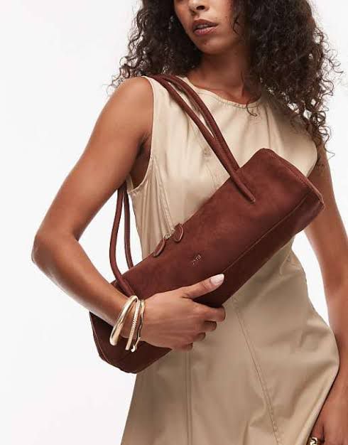 Woman holding a brown suede handbag against a plain background