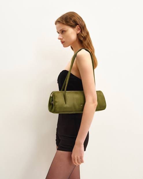Woman carrying a green handbag against a plain background.